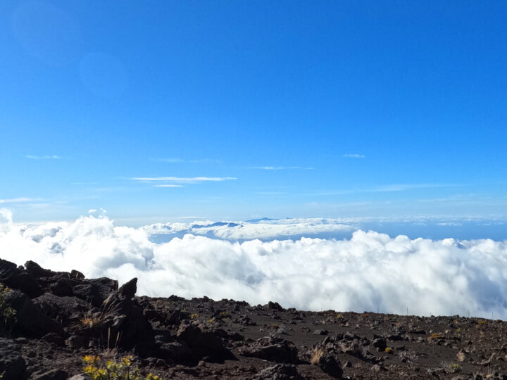 sunset Haleakala volcanic rock above clouds with horizon in distance with blue sky