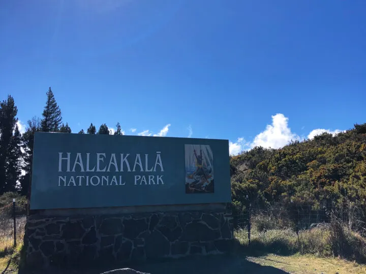 photo of Haleakala national park sign on sunny day with blue sky and trees surrounding it