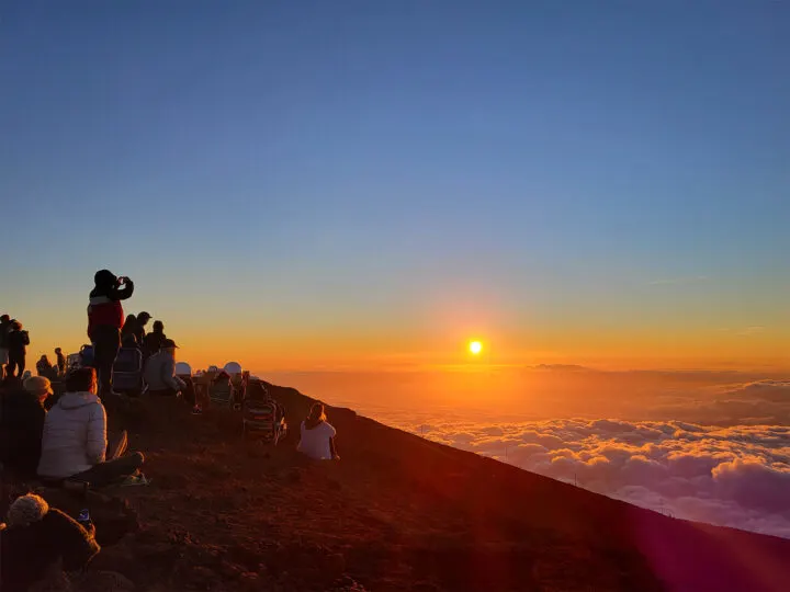 sunset Haleakala with people on side of mountain with clouds and orange sunset in distance