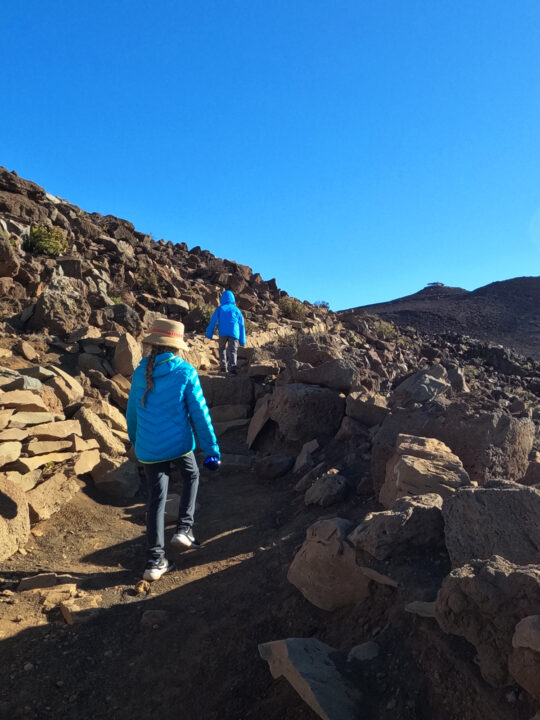 two kids in blue coats hiking up rocky terrain