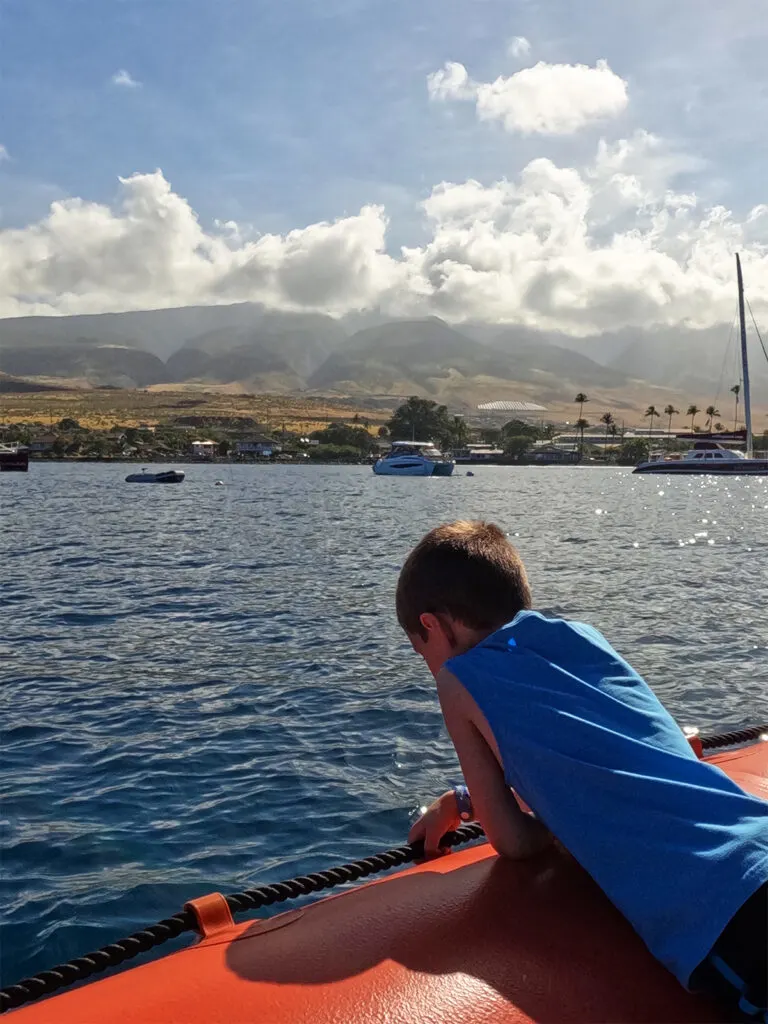 boy hanging over boat side with island of maui in distance