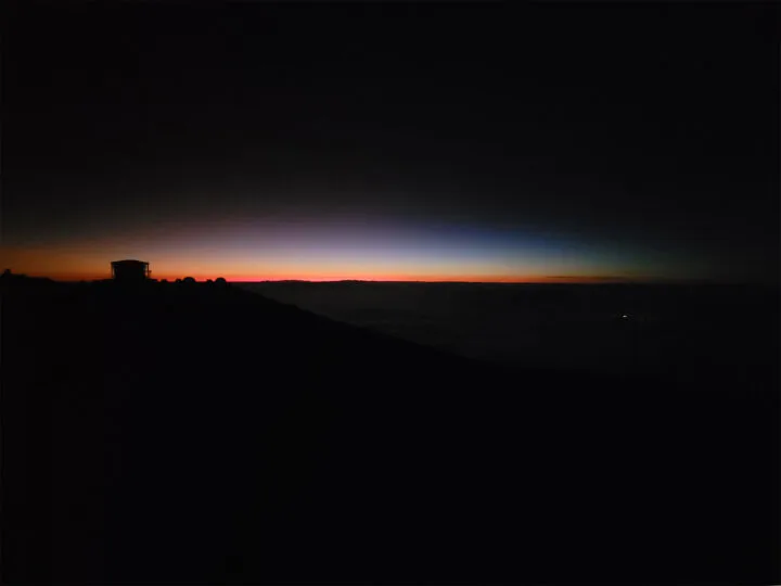 last sliver of light on Haleakala at sunset black photo with red blue an white line across horizon