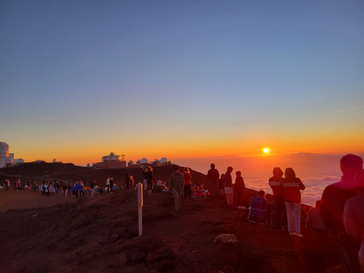 crowd of people standing atop Haleakala watching the sunset orange and blue sky