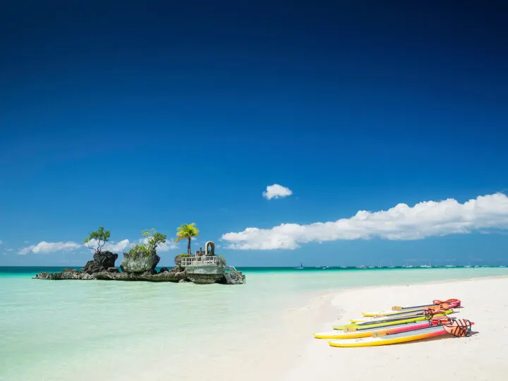 best beaches in December paddle boards on white sand at ocean with rocky structure in water