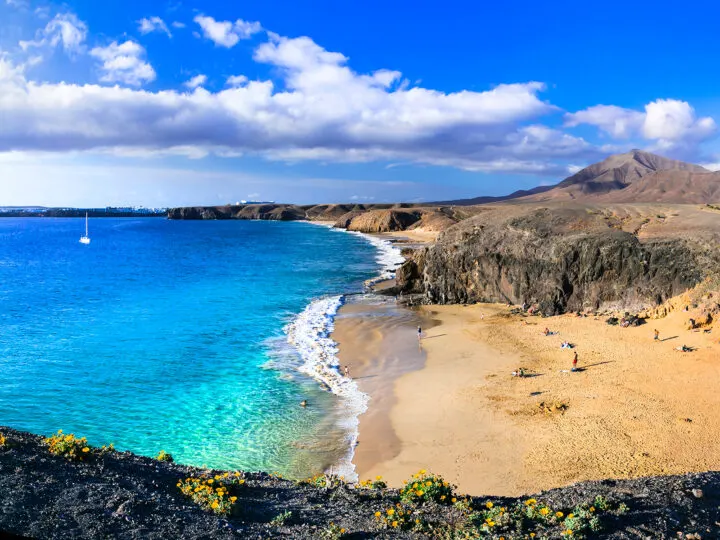 tan sand teal water with volcano in distance