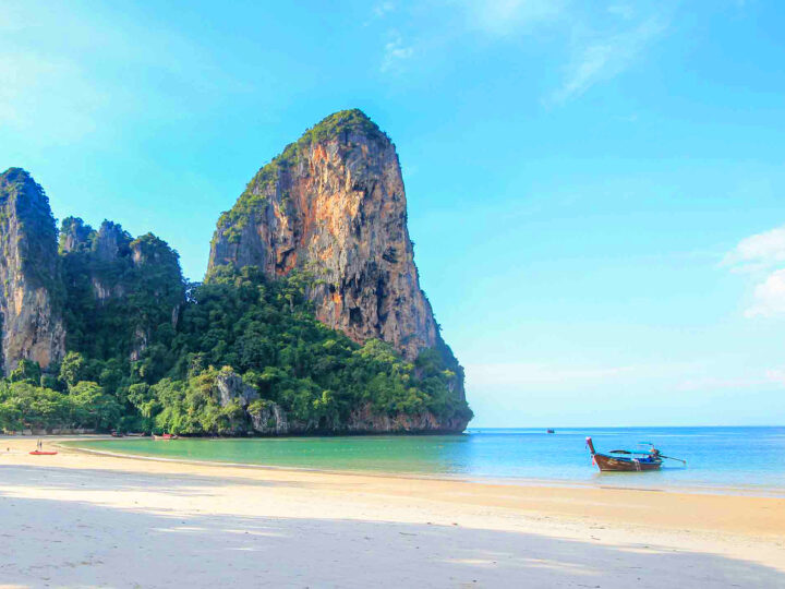 best tropical destinations in December view of Krabi with large rock formation boat on ocean and beach, Christmas vacation ideas