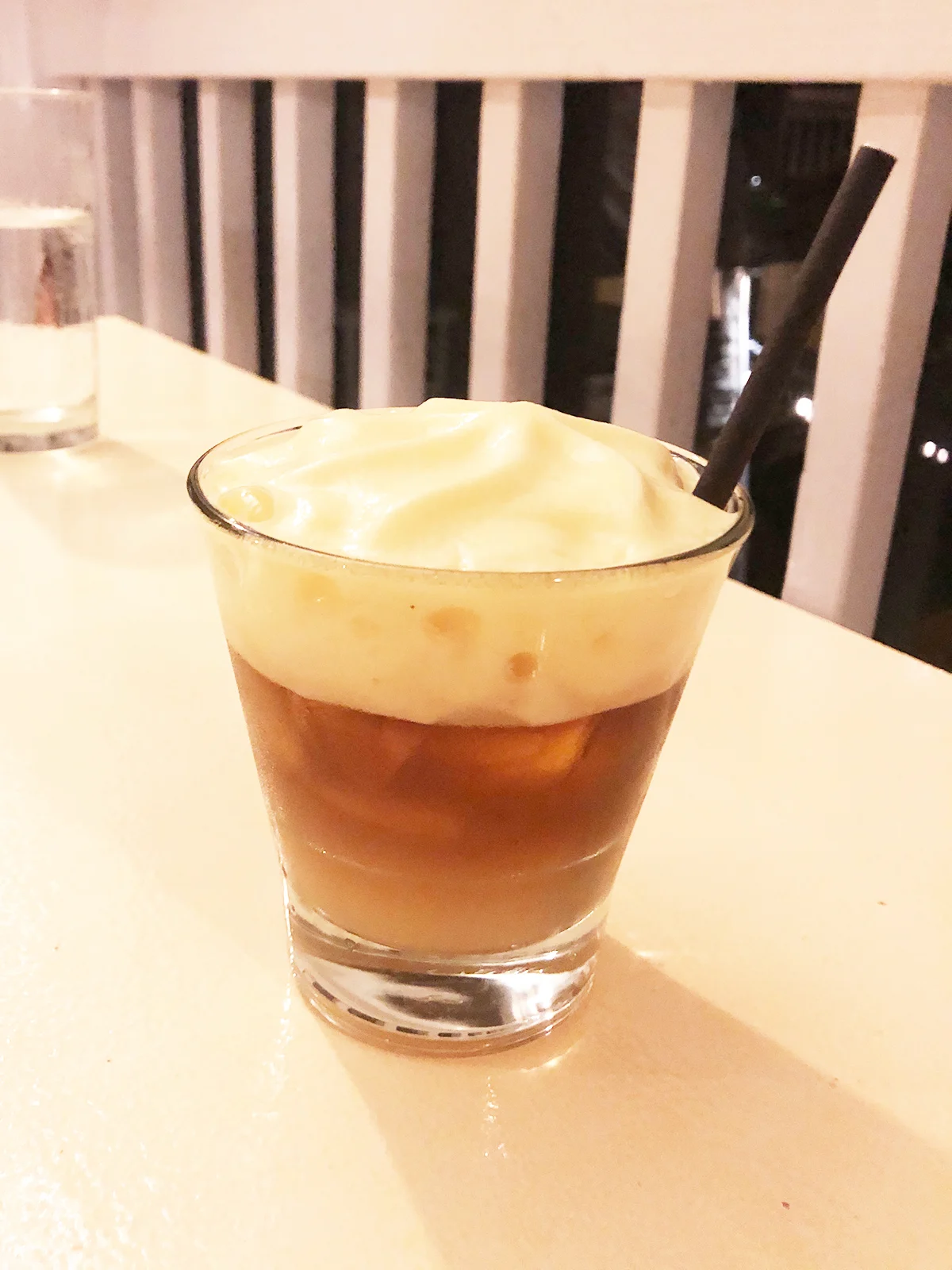 tan drink in glass with creamy foam on top with straw