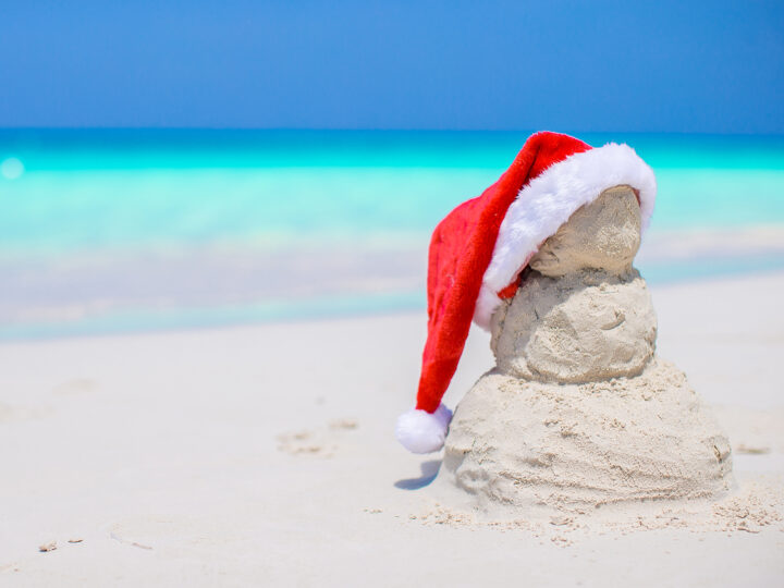 tropical Christmas best destinations photo of sand snowman with Santa hat and ocean in distance