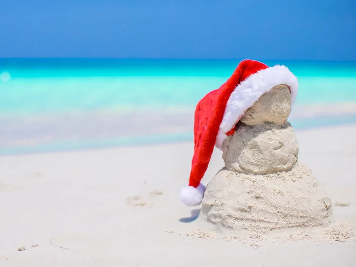 tropical Christmas best destinations photo of sand snowman with Santa hat and ocean in distance