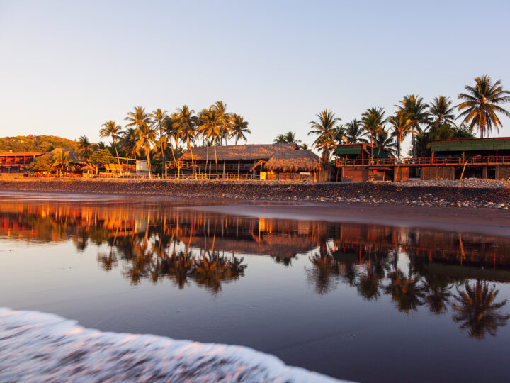 beach in El Salvador with black sand palm trees and buildings with reflection in waves