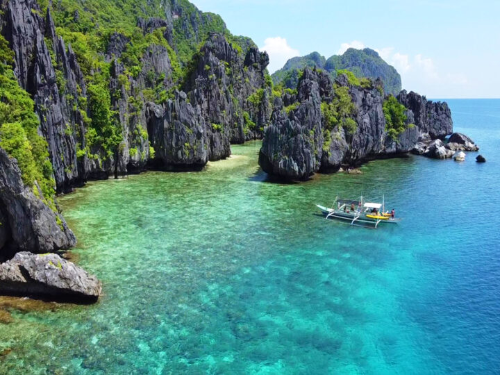 view of best places to visit in January for sun Philippines boat on blue water with rocky cliffs nearby