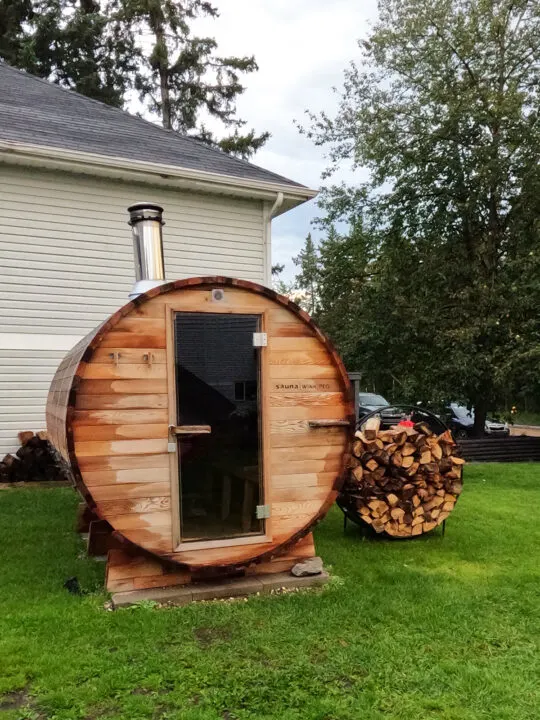 small stand alone sauna with wood next to it