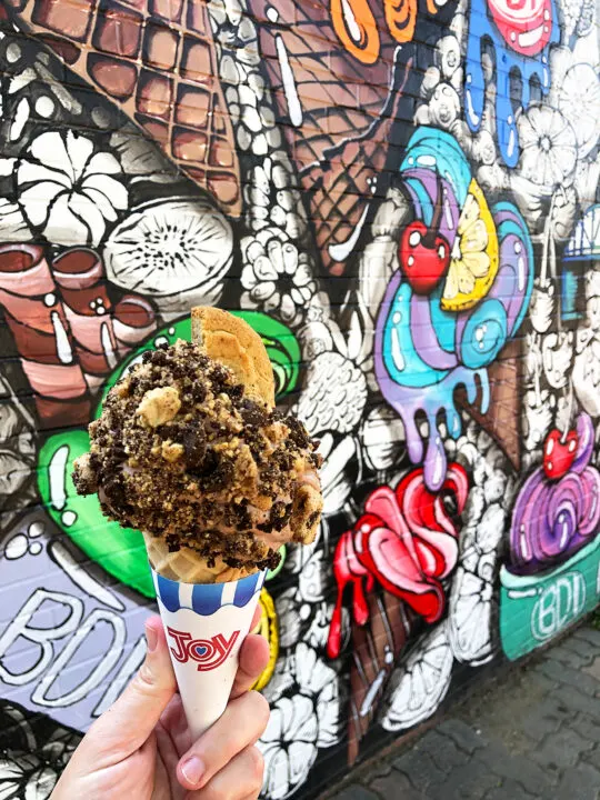 hand holding ice cream cone with colorful mural in distance