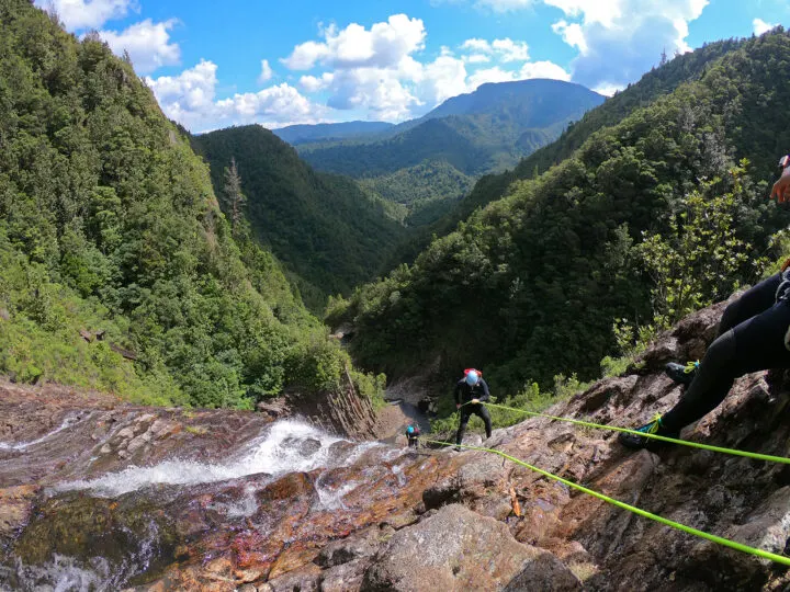 New Zealand best countries to visit in January view of landscape with people repelling down cliff with valley in distance