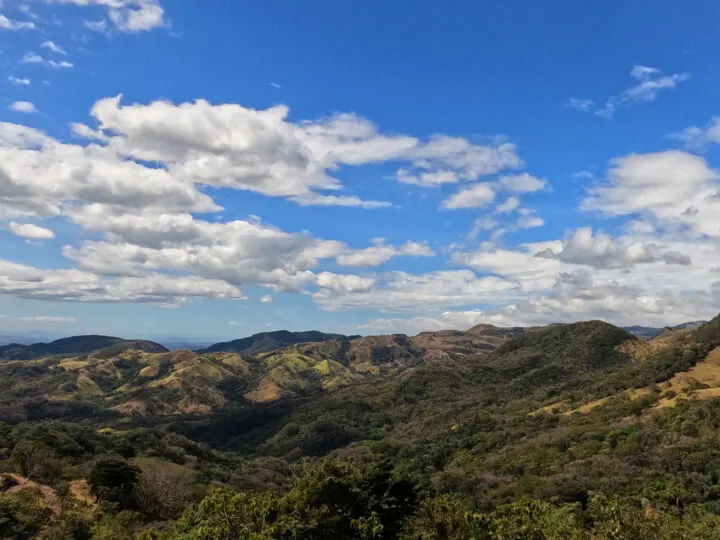 rolling hills with trees white puffy clouds in blue sky best Costa Rica itinerary