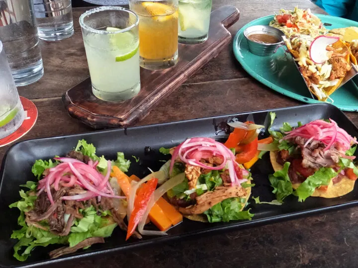 small tacos on plates with margaritas in background