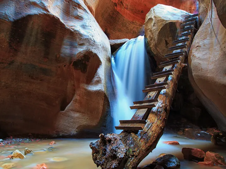 view of log with steps leading up to Kanarra falls in rocky slot canyon
