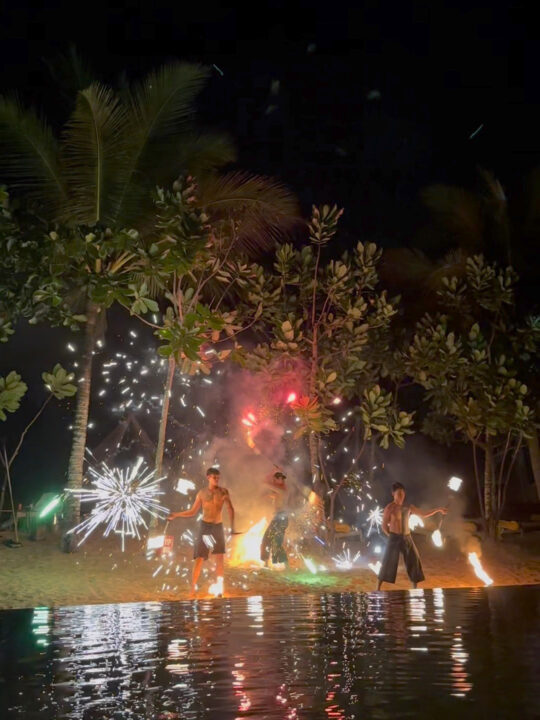 fire show khao lak view of three men holding fire with pool and palm trees