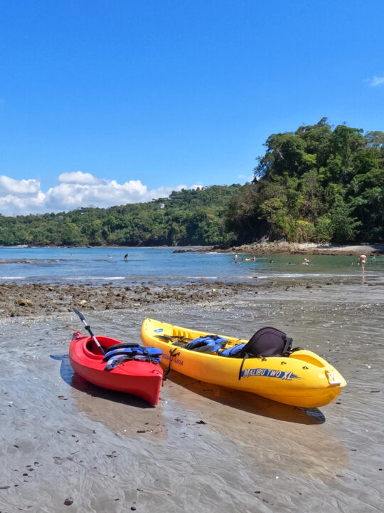 things to do in Manuel Antonio Costa Rica go kayaking red and yellow kayaks sitting on rocky beach with water and trees