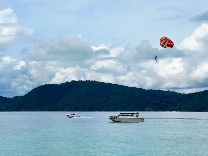 parasailing in Manuel Antonio things to do view of boat on blue water with guy parasailing and land in distance