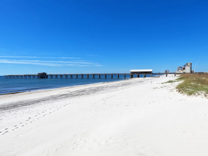 white sand blue water and sky with pier in alabama