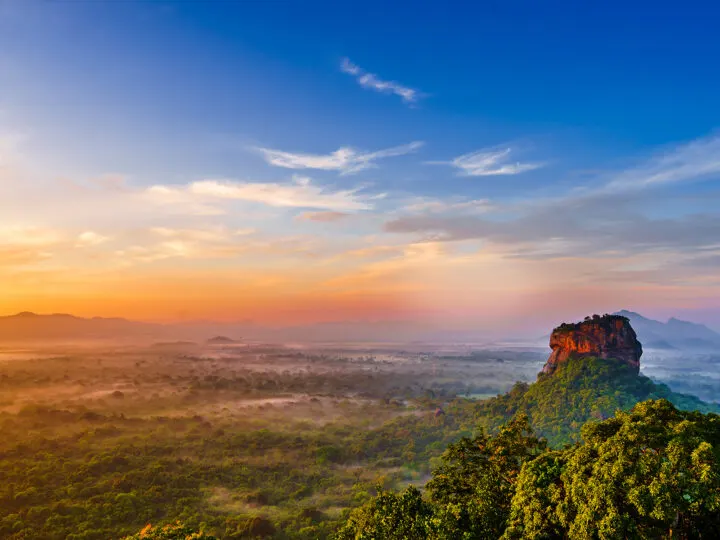 cheap spring break trips for families sunset at disk over jungle with large rock sticking through in Sri Lanka