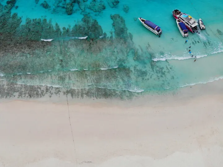 beach looking down at blue water with boats and white waves