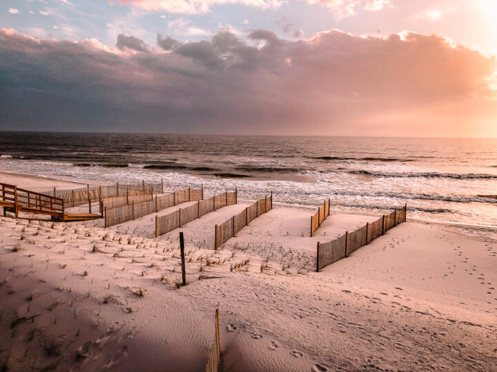 best vacation spots gulf coast view of pink beach at sunset with fences and footprints