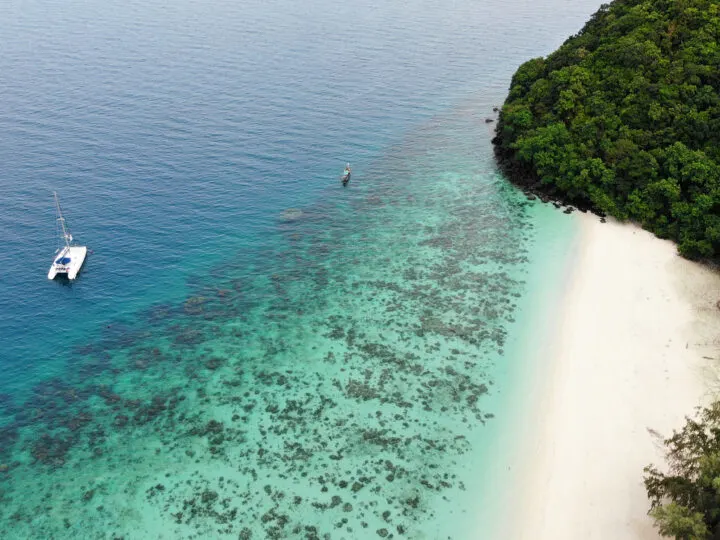coral island thailand from above white sand beach teal and blue water tropical trees white boat
