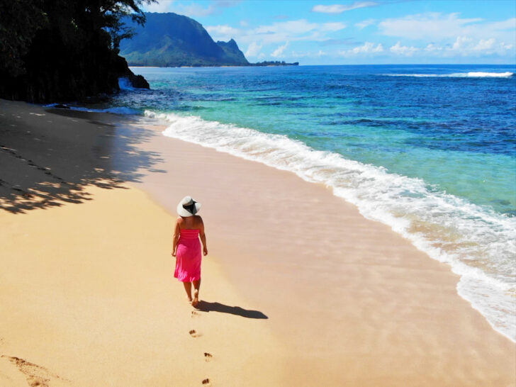 woman walking on beach with pink dress sun hat with coast and ocean in distance what to wear in Hawaii