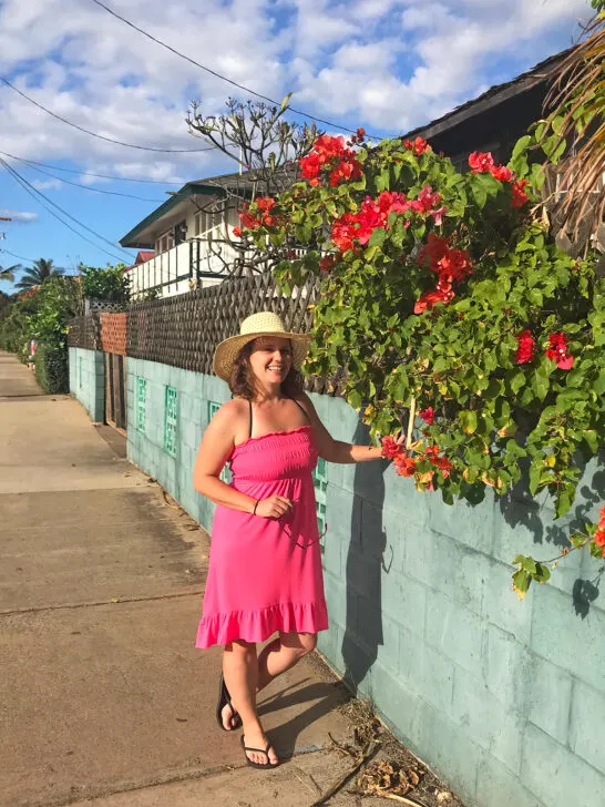 woman standing along brick wall with flowers wearing pink dress and sun hat