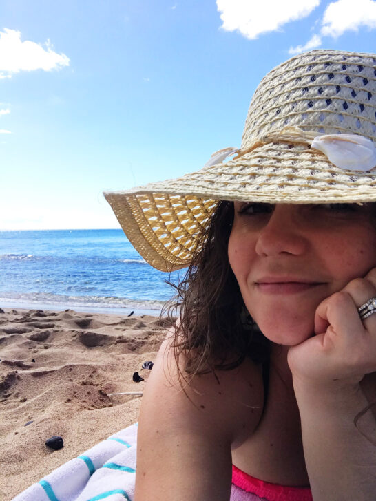 what to wear in hawaii view selfie of woman in beach hat laying on towel with ocean in background