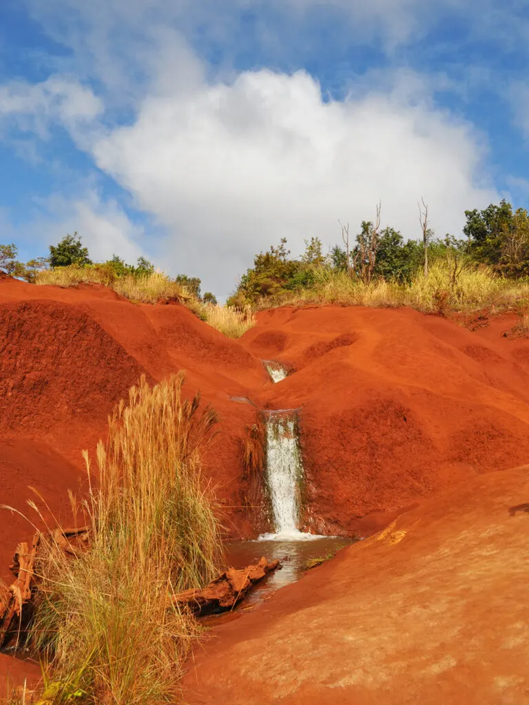 maui vs. kauai view of red sand with waterfall on sunny day