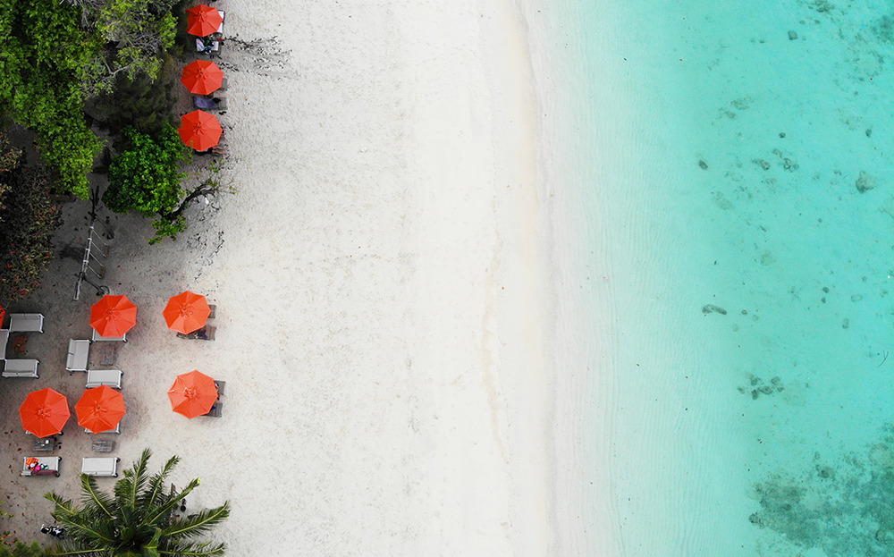 phuket thailand travel guide view of white sand beach orange umbrellas teal water looking down