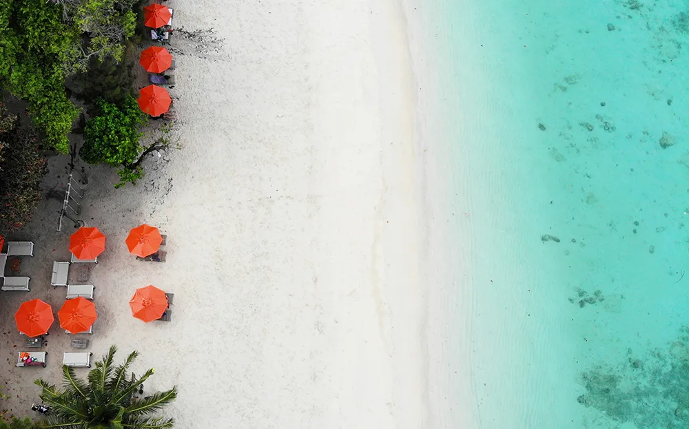 phuket thailand travel guide view of white sand beach orange umbrellas teal water looking down
