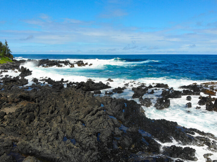 maui or kauai black rocks white waves blue water sunny day
