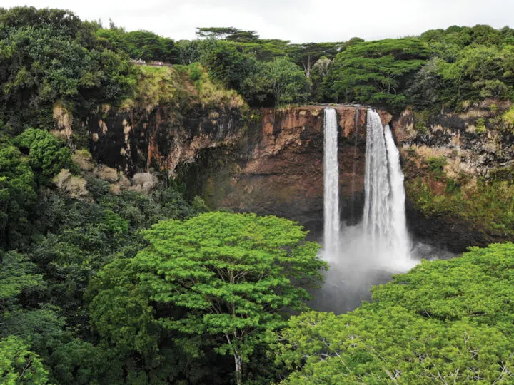 kauai vs. maui view of white waterfall and pond below with trees surrounding it