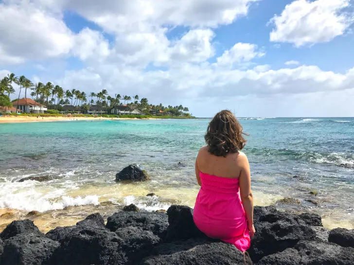 what to pack for hawaii list woman sitting on black rocks near ocean with coast in distance