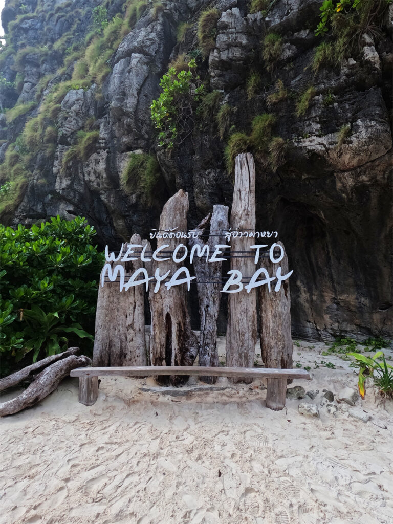 welcome to Maya bay sign with beach and rocky cliff behind