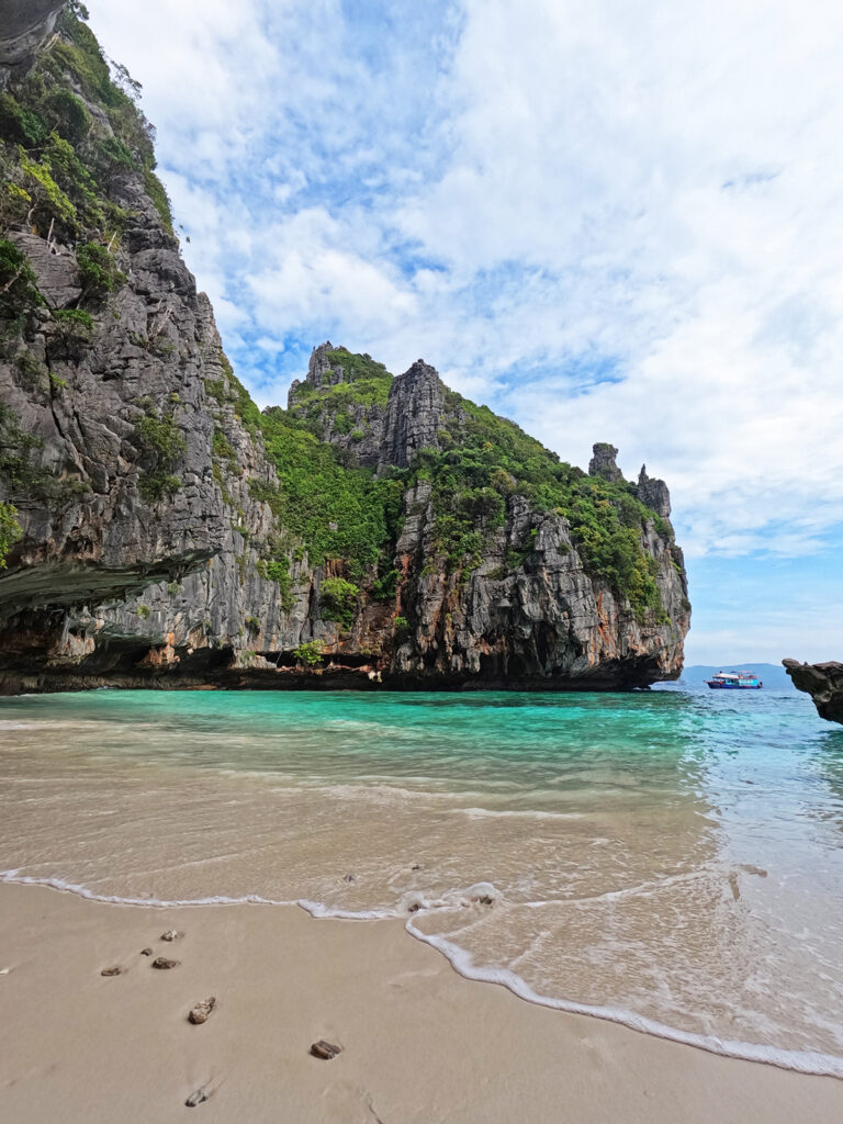 things to do in Phi Phi Islands view of empty beach cove with tan teal water and limestone cliffs