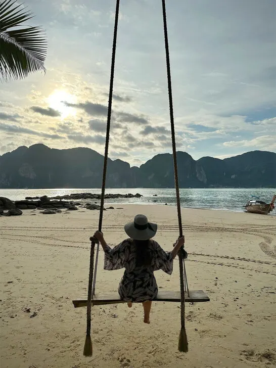 woman swinging on beach looking at mountains near sunset