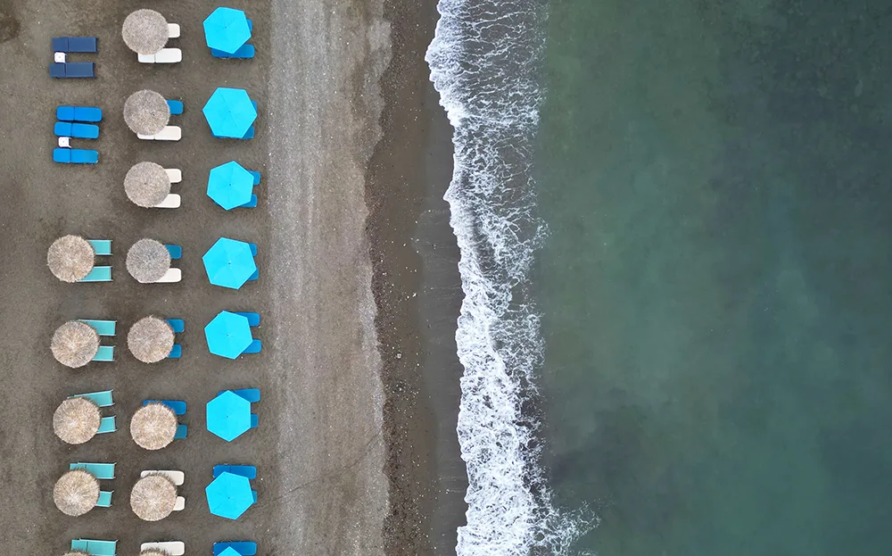 Crete Greece travel guides aerial view of beach with green water white wave blue and tan umbrellas