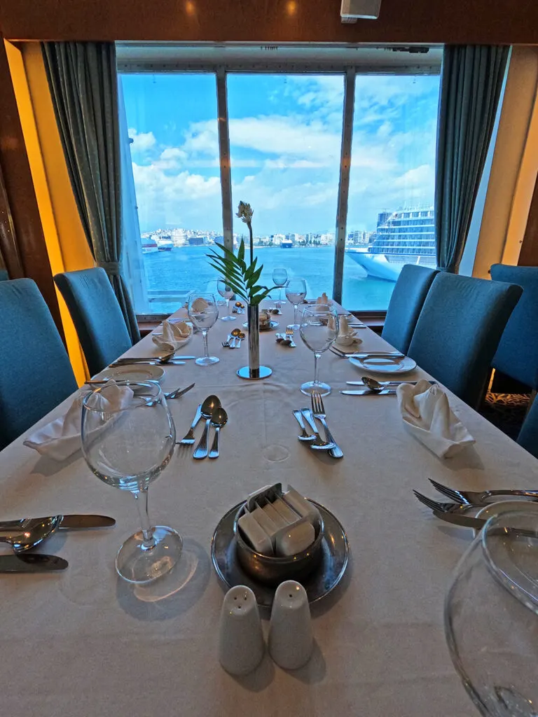 set dinner table with glasses flatware blue chairs and cruise ship through window