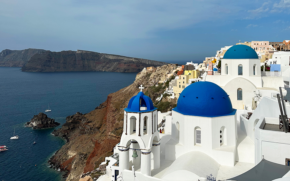 Greece travel guides view of Cyclades islands famous Santorini blue dome churches with Aegean Sea in distance