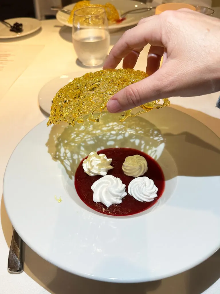 white dollops of cream in red dessert sauce with hand holding yellow topping