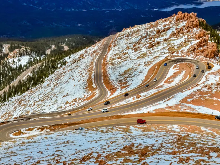 curvy mountain road with snow and red rock above tree line