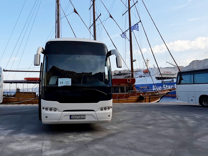 tour bus in Santorini in parking space with boat behind in harbor