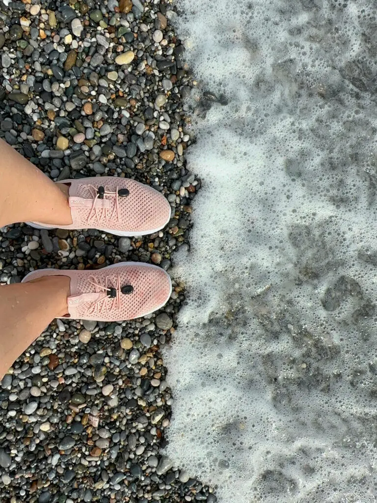 woman wearing pink water shoes on rocky beach with white wave