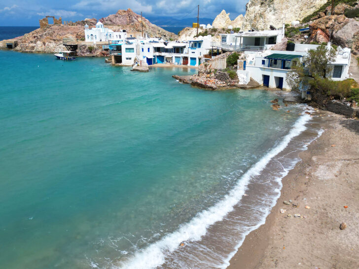couples holiday to Greece with view of teal water and beach with buildings beside it