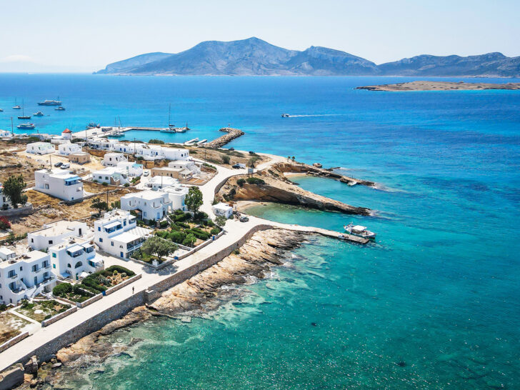 couples holiday to greece view of small island with white buildings along shore bright blue ocean water